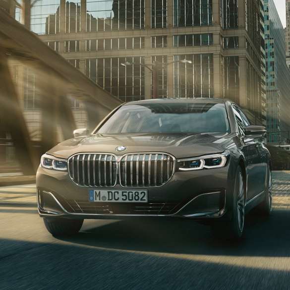BMW 7 серии Седан: системы помощи водителю Системы помощи водителю: BMW 7 серии Седан в движении на фоне городского пейзажа