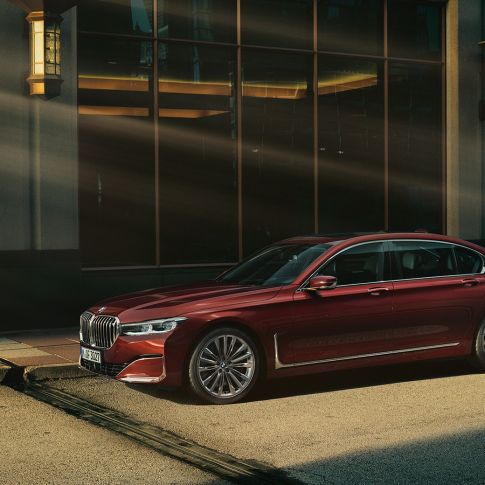 BMW 7 серии Седан Individual: вид сбоку BMW 7 серии Седан Individual красного цвета: вид сбоку на фоне городского пейзажа
