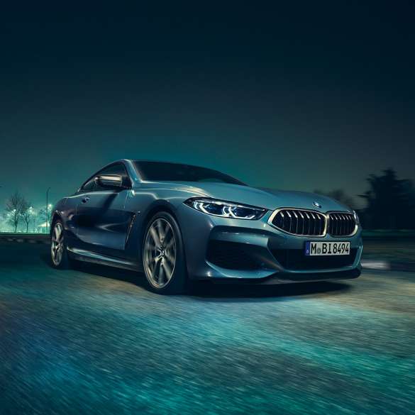 BMW M850i xDrive Coupé, вид спереди с поворотом в три четверти слева. BMW M850i xDrive Coupé в Barcelona Blue металлик, вид спереди с поворотом в три четверти слева, езда ночью.