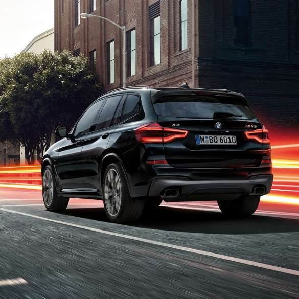 BMW X3 M40i, three-quarter rear view. BMW X3 M40i in Black Sapphire metallic, driving, exterior, three-quarter rear view before an urban background with light strips.