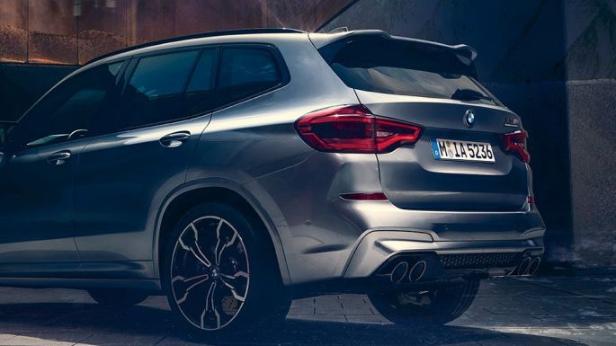 BMW X3 M Competition, lateral rear view. BMW X3 M Competition in Donington Grey metallic, exterior, lateral rear view with two people in the foreground.