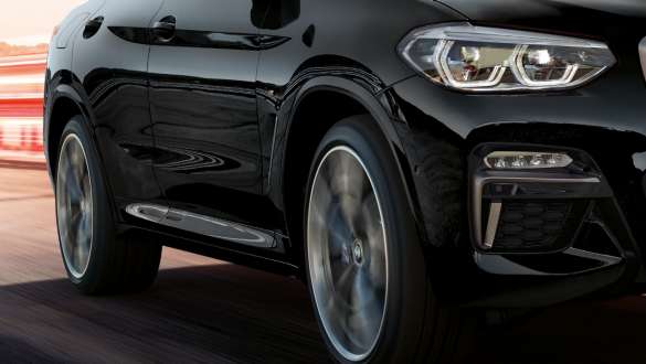 BMW X4 M40i и BMW X4 M40d, вид сбоку с поворотом в три четверти. BMW X4 M40i и BMW X4 M40d в Black Sapphire металлик, за рулем, экстерьер, вид сбоку с поворотом в три четверти с крутящимися легкосплавными дисками.