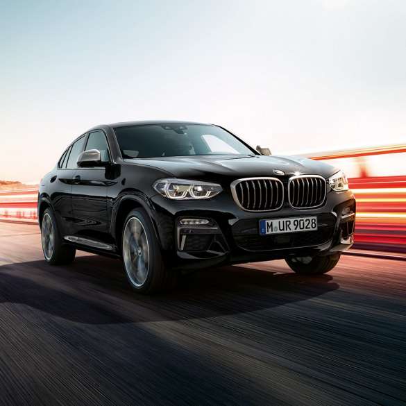 BMW X4 M40i, вид сзади с поворотом в три четверти. BMW X4 M40i в Black Sapphire металлик, за рулем, экстерьер, вид сзади с поворотом в три четверти со световыми полосками.