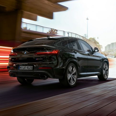 BMW X4 M40i, вид сзади с поворотом в три четверти. BMW X4 M40i в Black Sapphire металлик, экстерьер, вид сзади с поворотом в три четверти, правая сторона со световыми полосками.