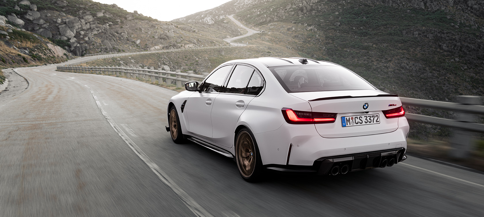 BMW M3 CS G80, вид сзади в три четверти в движении BMW M3 CS G80, вид сзади в три четверти в движении по дороге в горах