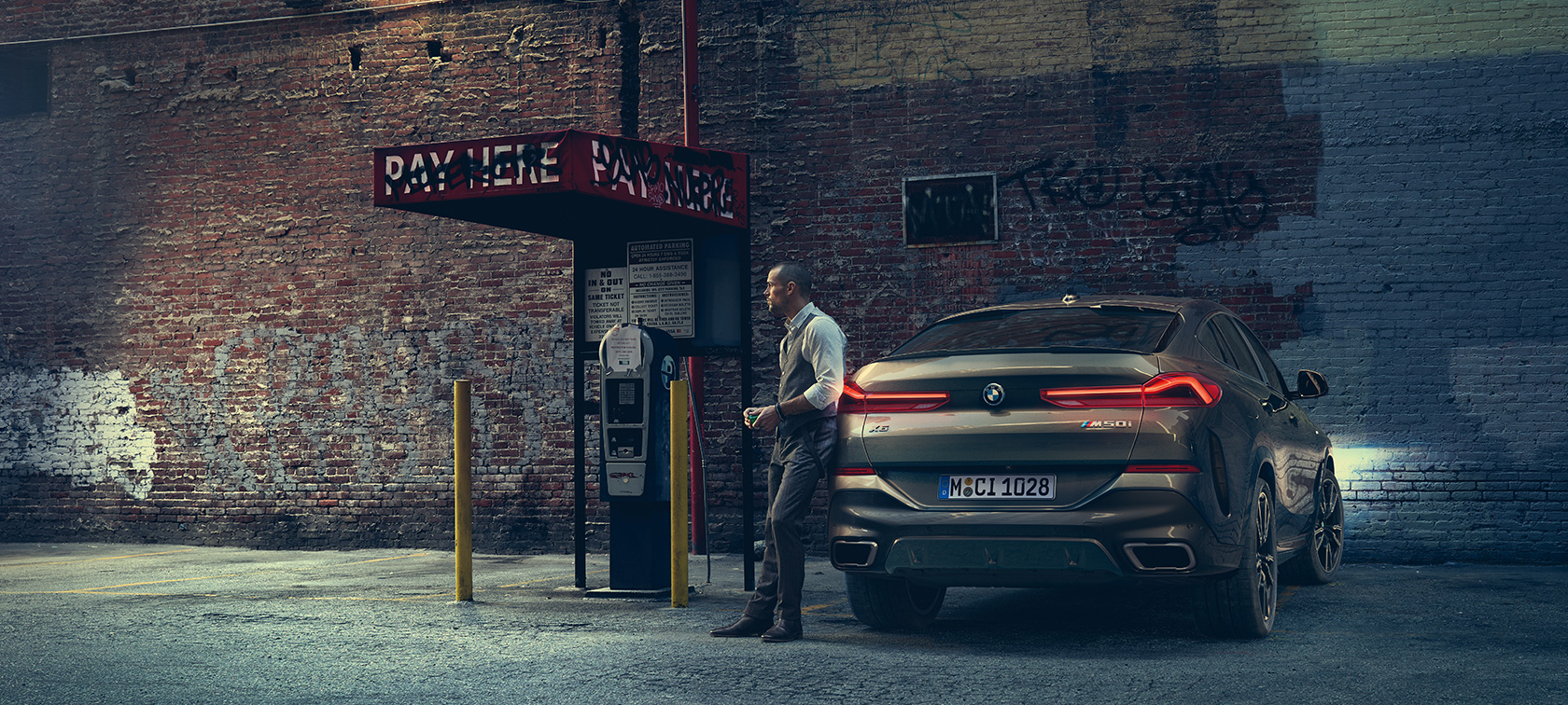 Задняя часть BMW X6 M50i. Мужчина опирается на заднюю часть BMW X6 M50i.