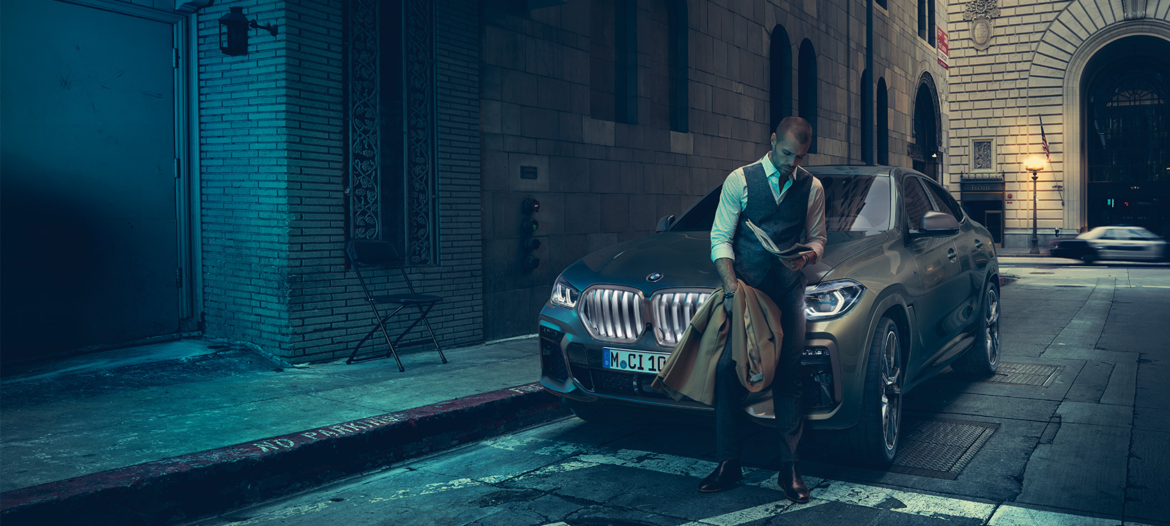 Передняя часть BMW X6 M50i. Мужчина опирается на переднюю часть BMW X6 M50i.