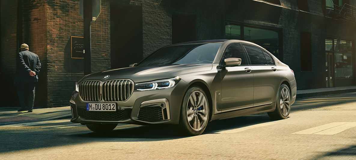 BMW M760Li xDrive Седан G11 G12 2019 в цвете Frozen Dark Silver metallic, вид на три четверти сзади, езда в городских условиях. BMW M760Li xDrive Седан G11 G12 2019 в цвете Frozen Dark Silver metallic, вид на три четверти сзади, езда в городских условиях.