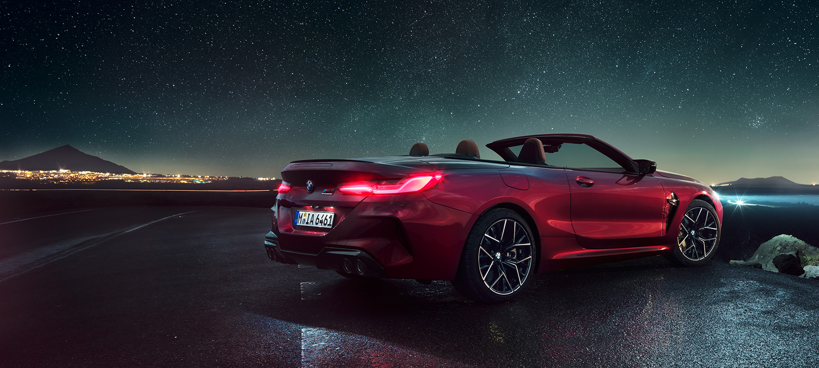 BMW M8 Competition Кабриолет, вид сзади с поворотом в три четверти. BMW M8 Competition Кабриолет в Motegi Red металлик с открытым мягким верхом, вид сзади с поворотом в три четверти, под звездным небом.