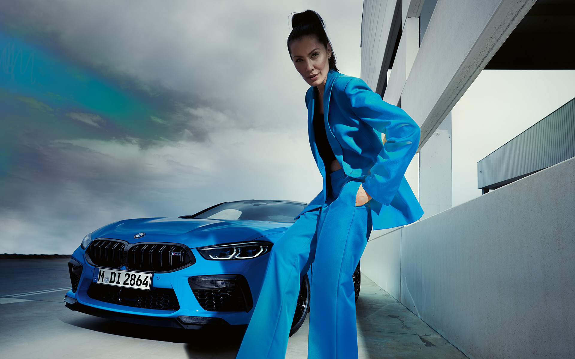 BMW M8 Competition Coupé F92 LCI (рестайлинг 2022 года) вид спереди с поворотом в три четверти BMW M8 Competition Coupé F92 LCI (рестайлинг 2022 года), Синий Дейтона-Бич, вид спереди с поворотом в три четверти с женщиной в синем костюме