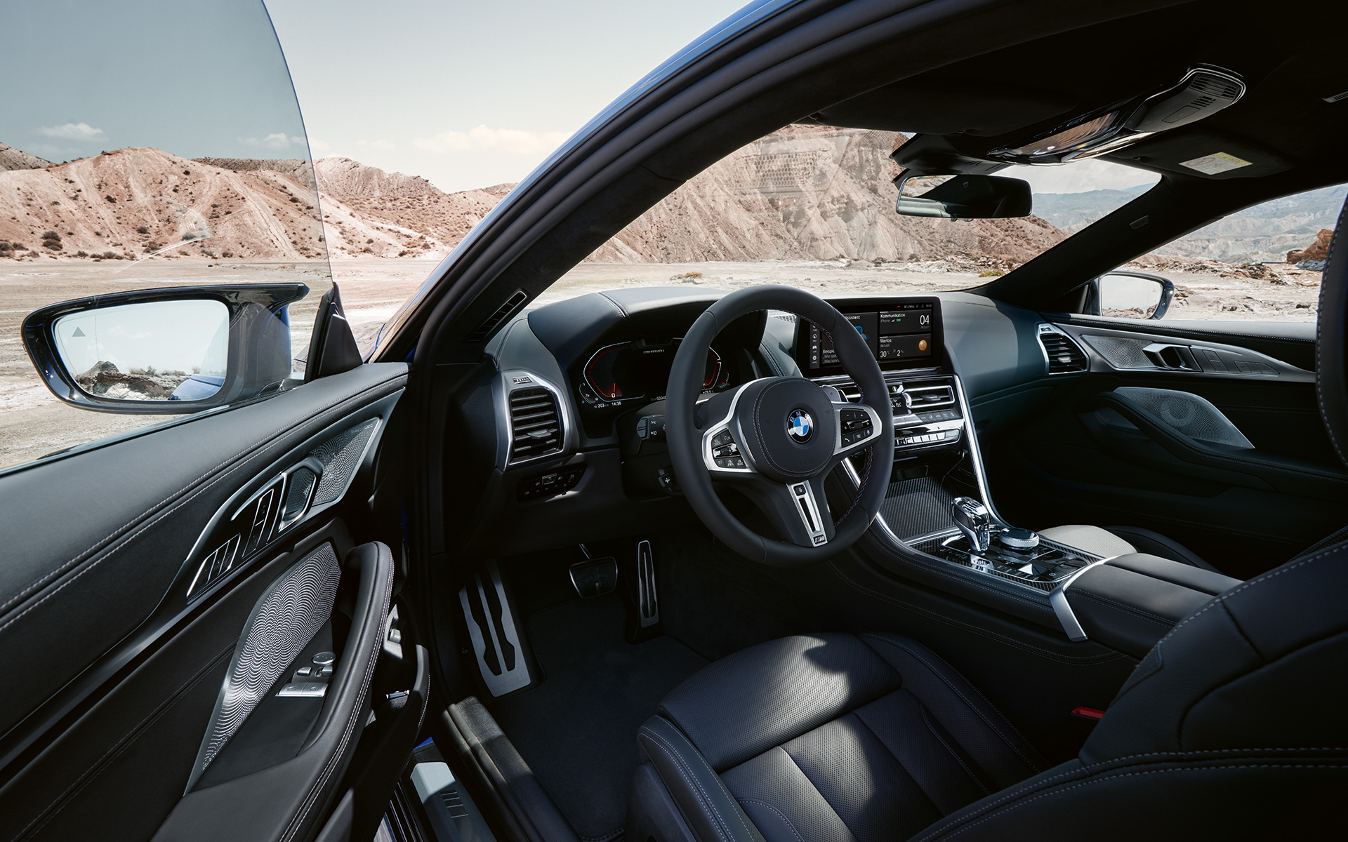 BMW M850i xDrive Coupé G15 LCI (рестайлинг 2022 года), ориентированный на водителя кокпит с кожаным рулевым колесом M BMW M850i xDrive Coupé G15 LCI (рестайлинг 2022 года), ориентированный на водителя кокпит с кожаным рулевым колесом M и открытой передней дверью