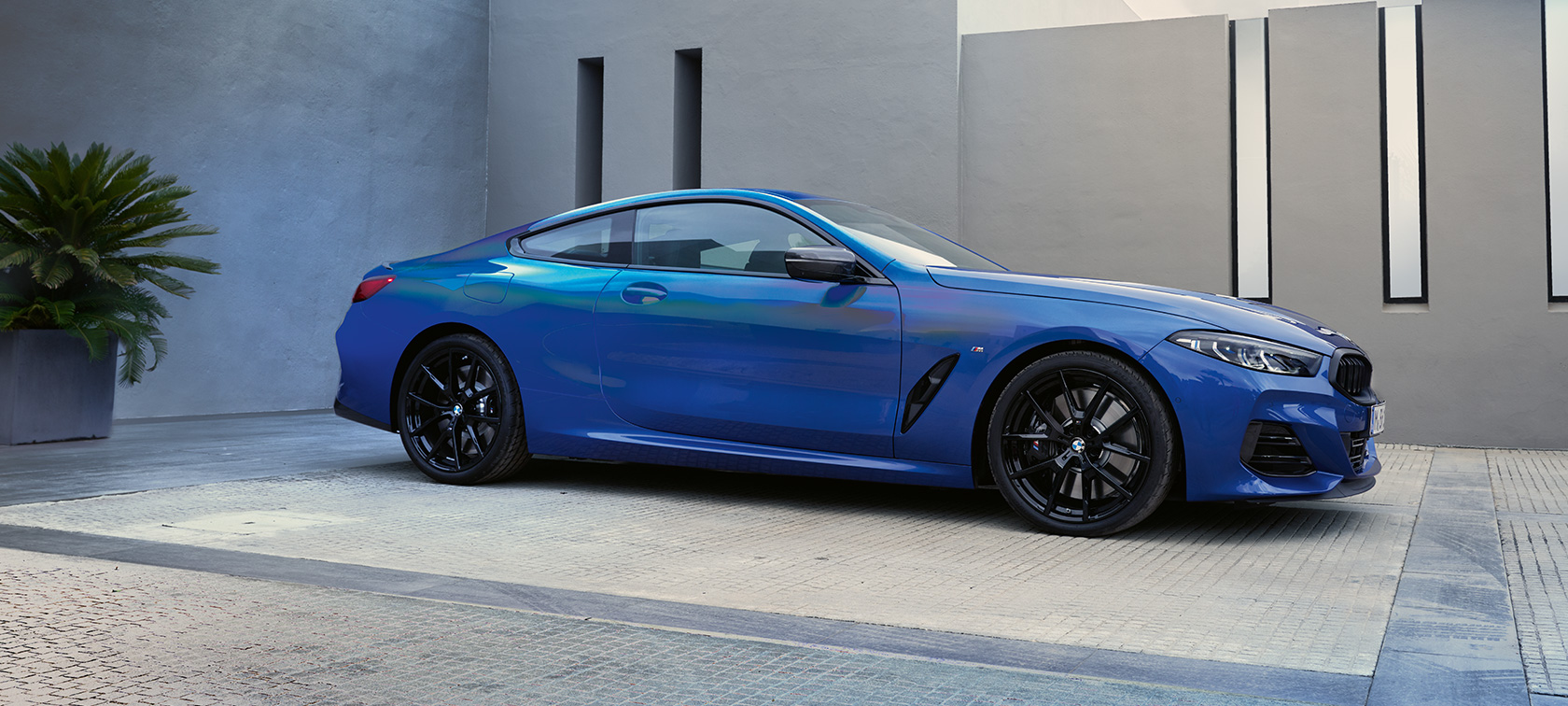 Вид сбоку BMW M850i xDrive Coupé G15 LCI (рестайлинг 2022 года) BMW M850i xDrive Coupé G15 LCI (рестайлинг 2022 года) M Синий Портимау металлик, вид сбоку перед зданием