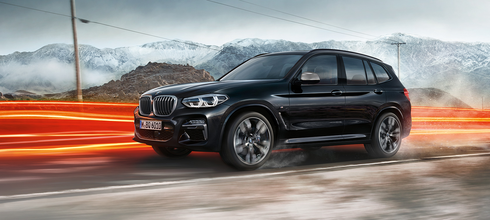 BMW X3 M40i и BMW X3 M40d, вид сбоку. BMW X3 M40i и BMW X3 M40d в Black Sapphire металлик, за рулем, экстерьер, вид сбоку перед горным пейзажем со световыми полосами.