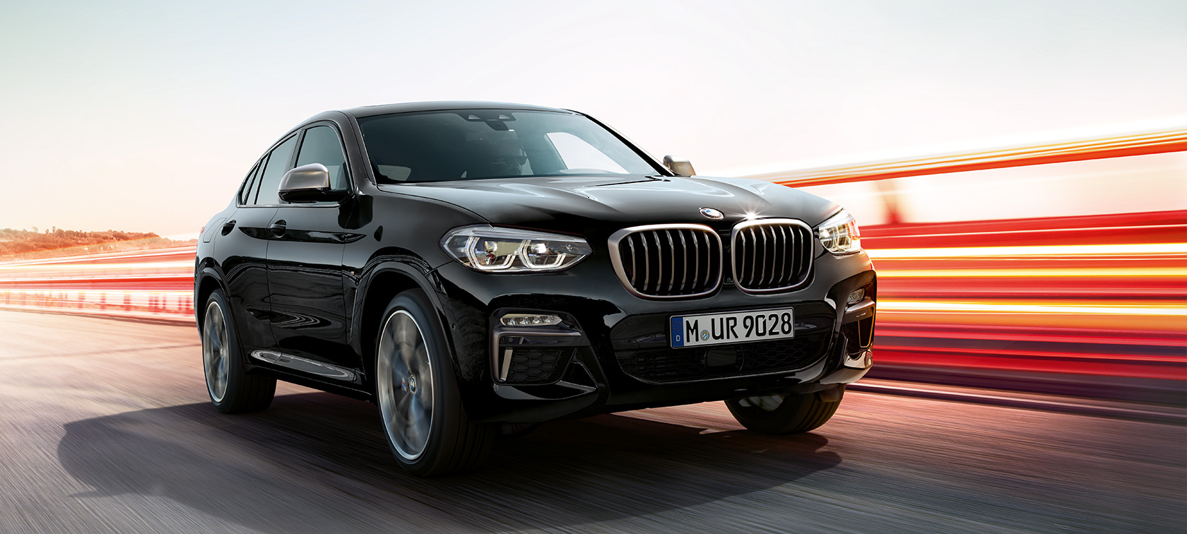 BMW X4 M40i и BMW X4 M40d, вид спереди с поворотом в три четверти, левая сторона. BMW X4 M40i и BMW X4 M40d в Black Sapphire металлик, экстерьер, вид спереди с поворотом в три четверти, левая сторона, со световыми полосами.