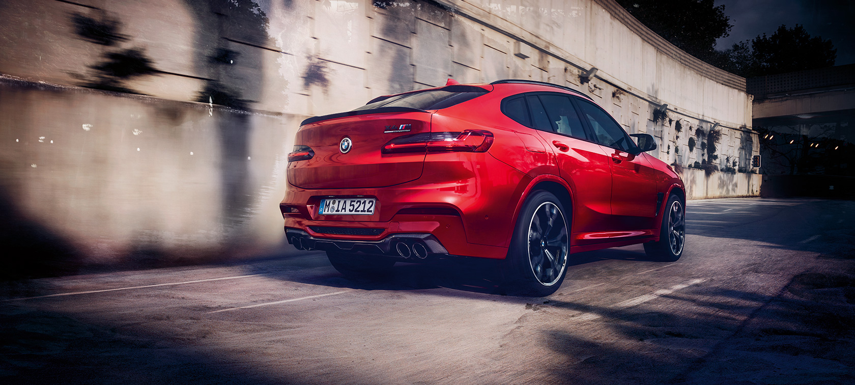 BMW X4 M Competition, вид сзади с поворотом в три четверти. BMW X4 M Competition в Toronto Red металлик, за рулем, экстерьер, вид сзади с поворотом в три четверти.