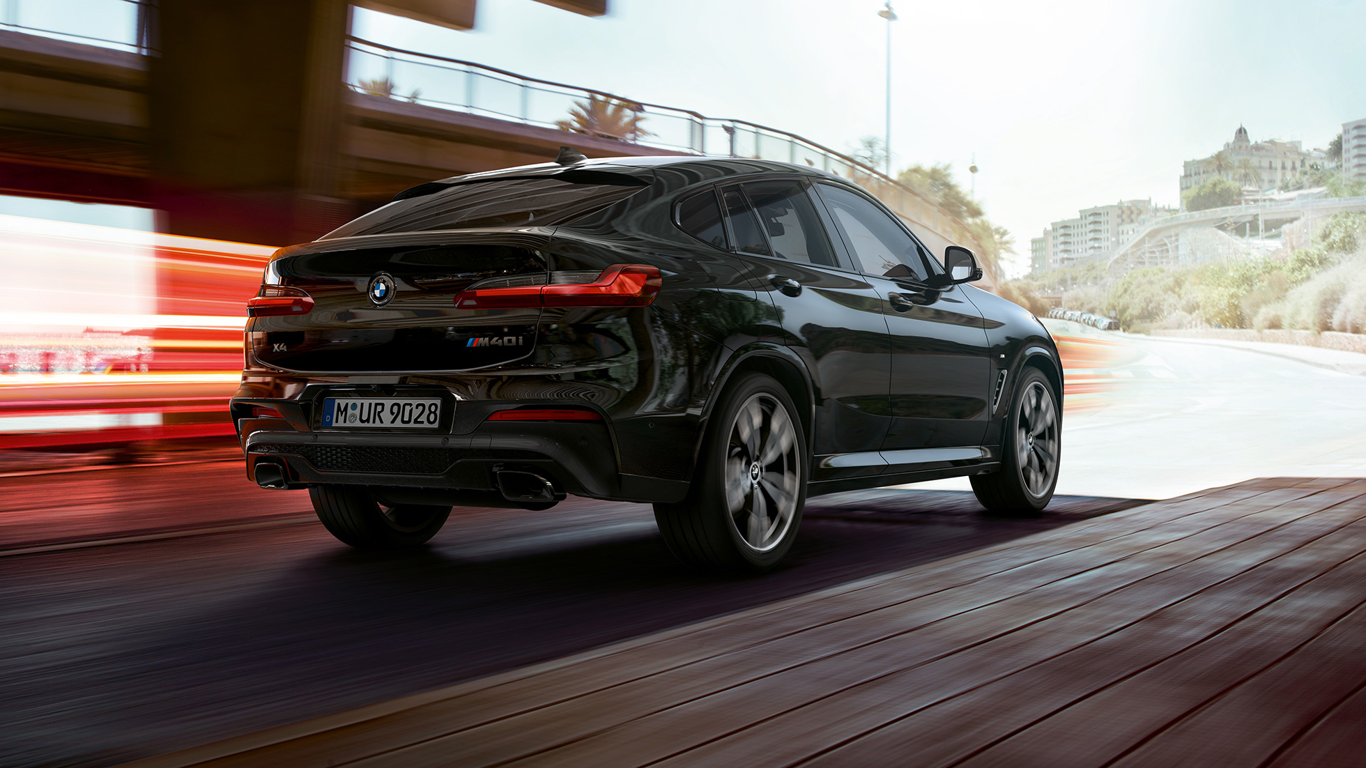 BMW X4 M40i, вид сзади с поворотом в три четверти. BMW X4 M40i в Black Sapphire металлик, экстерьер, вид сзади с поворотом в три четверти, правая сторона со световыми полосками.