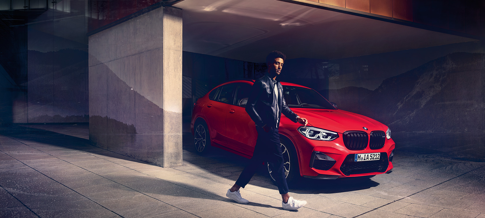 BMW X4 M Competition в Toronto Red металлик, экстерьер, вид сбоку с поворотом в три четверти с молодым человеком.