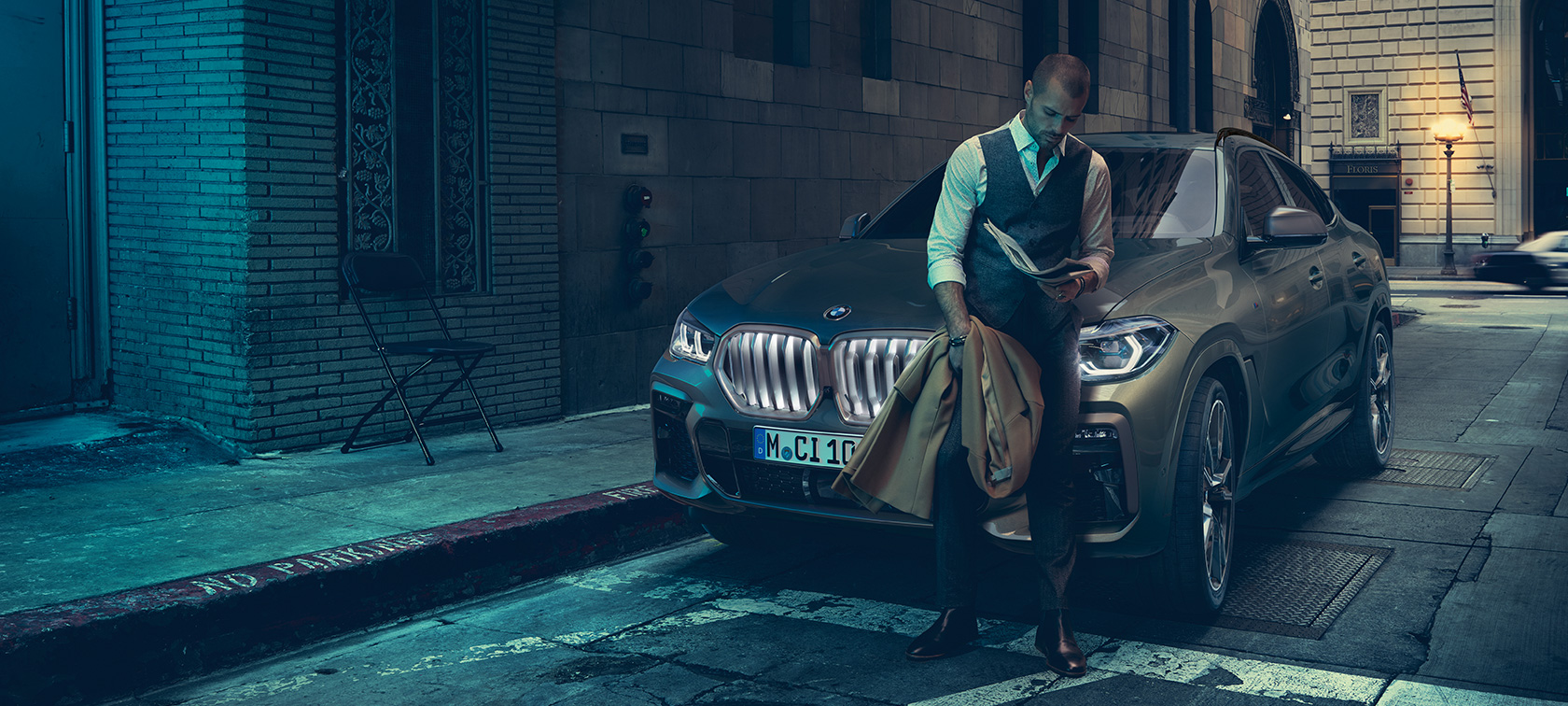 Человек опирается на BMW X6. Мужчина опирается на BMW X6 в боковой перспективе перед городской обстановкой.